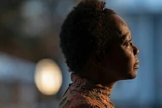 Profile of a black woman with an updo, wearing a patterned top against a blurred background, creating a soft, contemplative portrait.