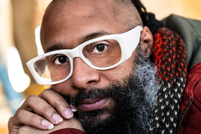 Close-up portrait of a black man with thick white glasses and beard, photographed by Doug Menuez