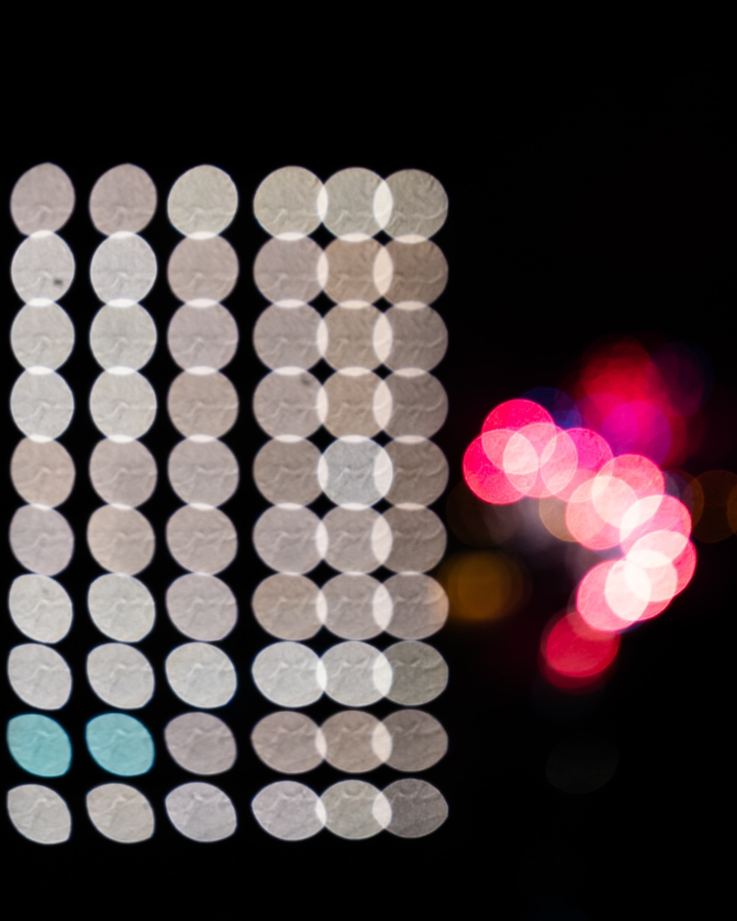 Abstract image showing an arrangement of luminous white, blue, and pink bokeh circles against a dark background, creating a visually striking pattern.