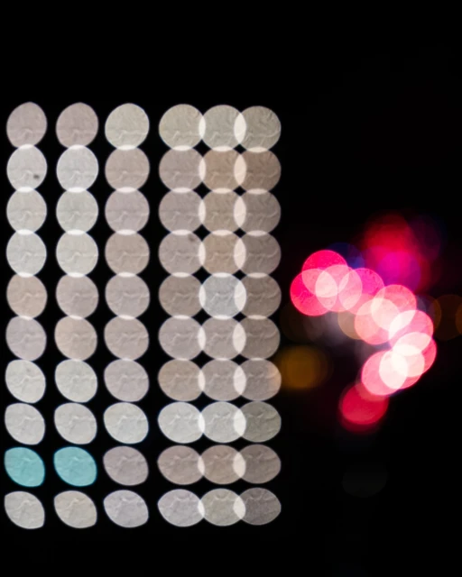 Abstract image showing an arrangement of luminous white, blue, and pink bokeh circles against a dark background, creating a visually striking pattern.
