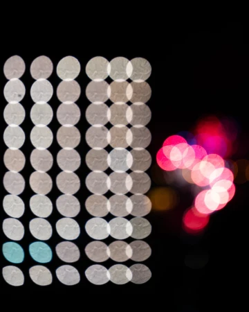 Abstract image showing an arrangement of luminous white, blue, and pink bokeh circles against a dark background, creating a visually striking pattern.