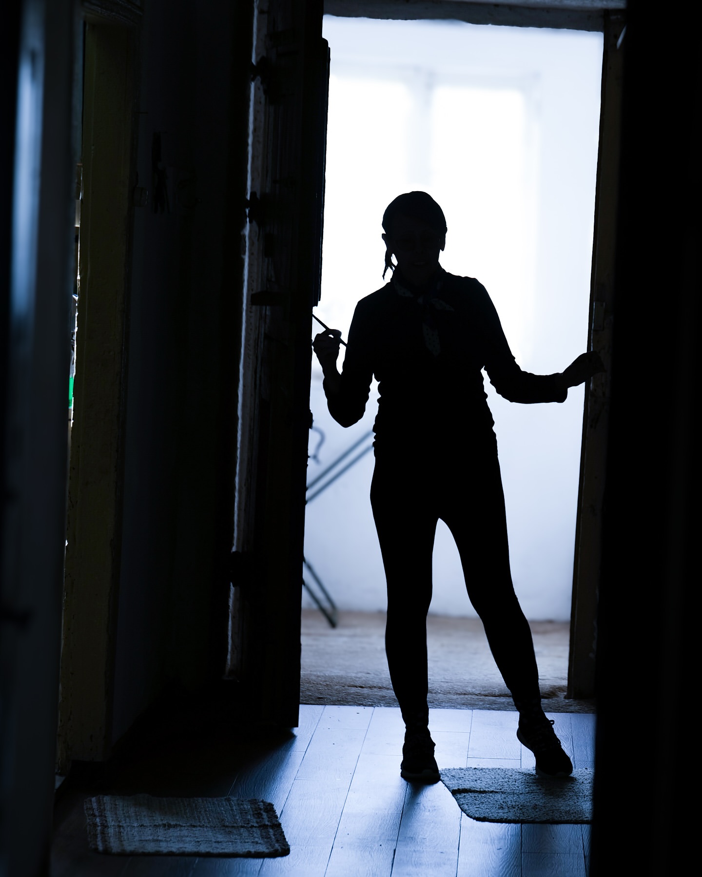 Silhouette of an adult female standing in a doorway with a blurred background, creating a dark and mysterious atmosphere.