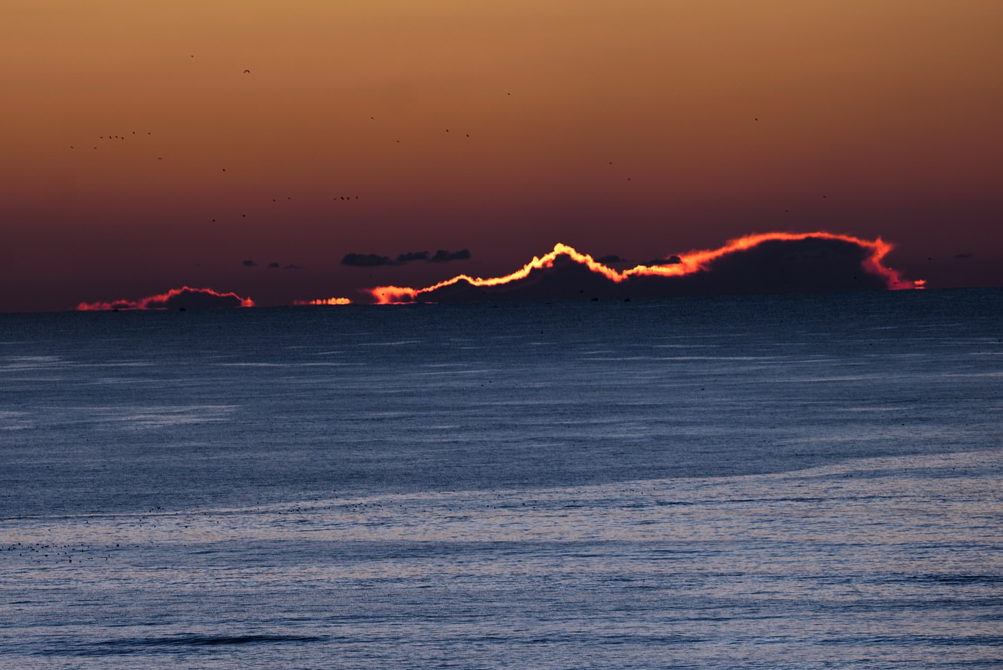 Scenic ocean landscape at sunset, featuring a colorful sky and rippling water with distant dark clouds on the horizon.