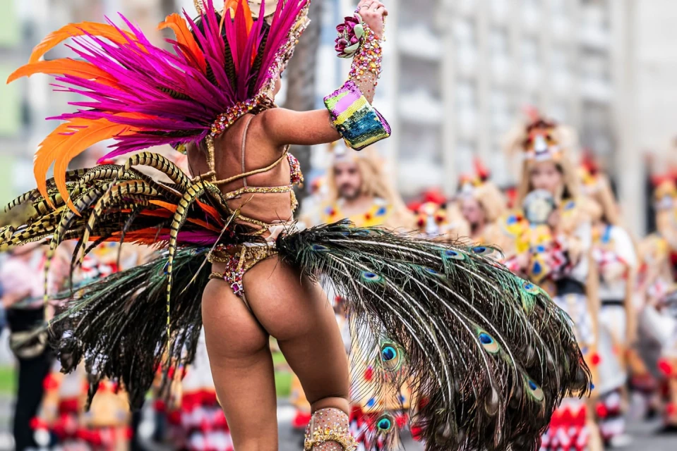 Adult female in a colorful Carnival costume with orange and fuchsia feathers and peacock feathers, parades in a city street.