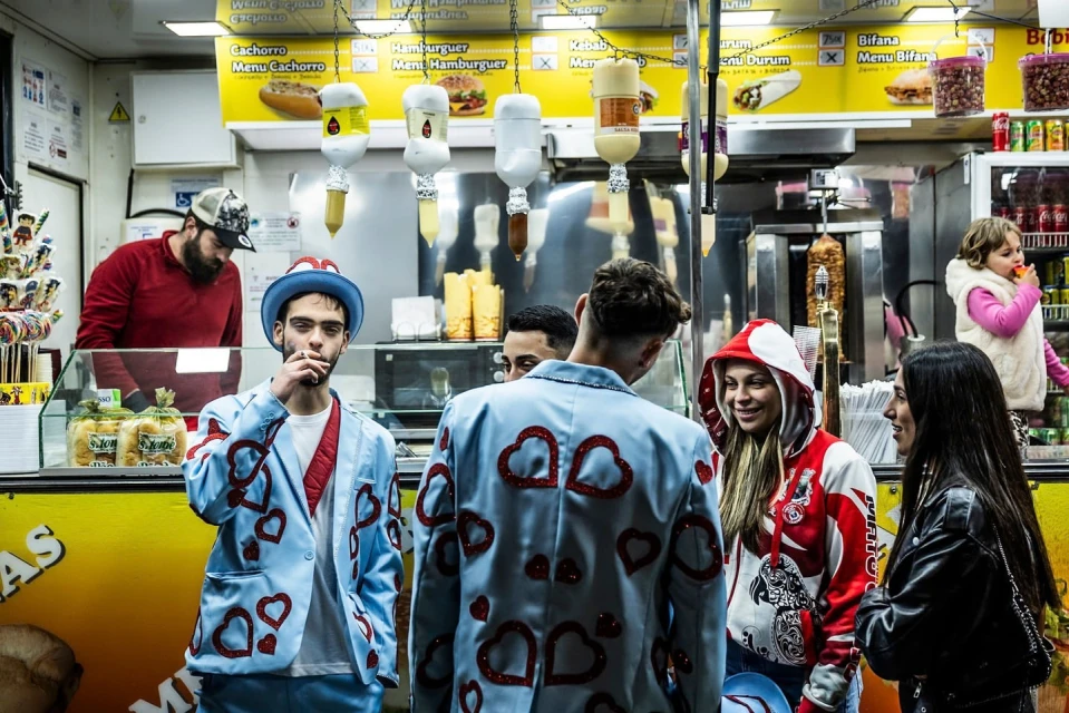 Group of people near a food stand with various food options displayed on the menu, capturing a social moment with diverse attire.