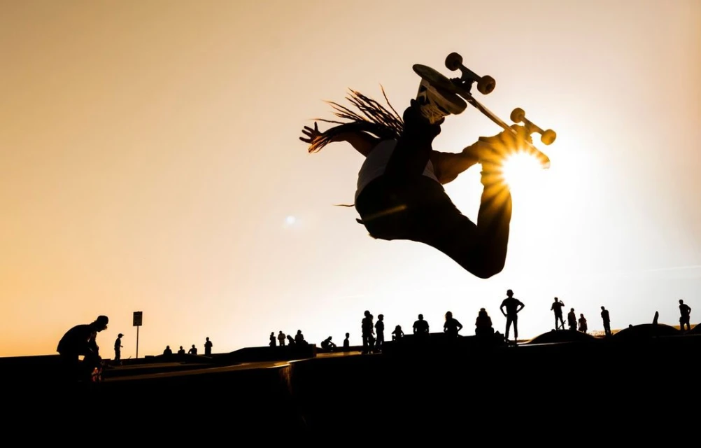 Silhouette of a skateboarder performing a trick in the air, with a group of silhouetted people in the background against a sunset sky.