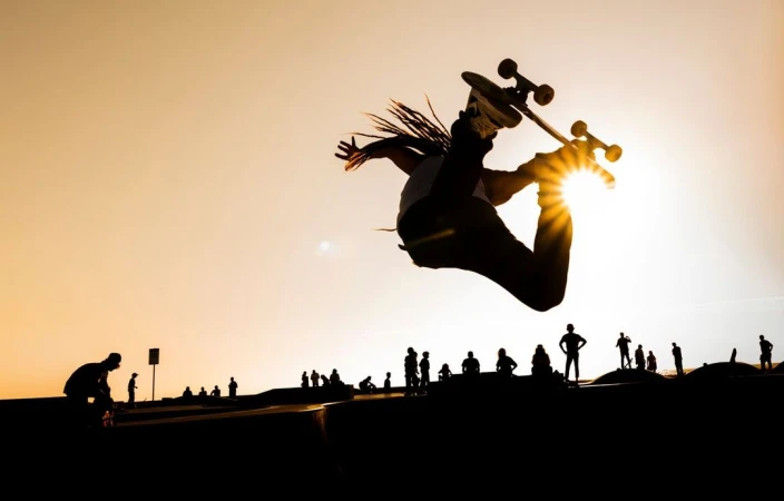 Silhouette of a skateboarder performing a trick in the air, with a group of silhouetted people in the background against a sunset sky.