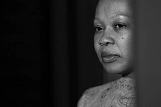 Close-up monochrome portrait of a Black woman looking thoughtfully off-camera, photographed by Doug Menuez