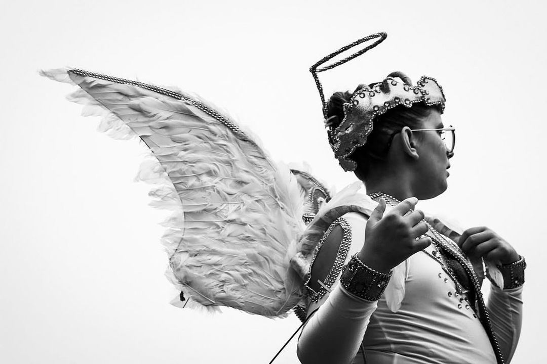 Monochrome shot of a person in angel costume with wings and halo. The individual is looking off to the side in an outdoor setting.