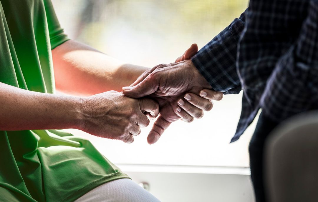 Close-up of two people holding hands, one in green shirt, other in plaid shirt, conveying support and connection.