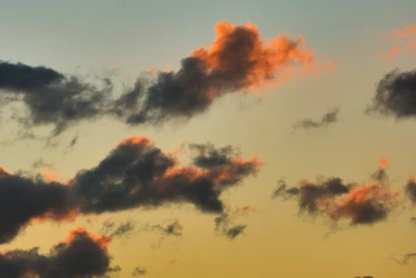 Dramatic sunset sky with dark gray clouds illuminated by warm orange light.