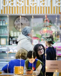 People seated inside a pastelaria past a window with hanging fairy lights and printed signage, photographed by Doug Menuez.