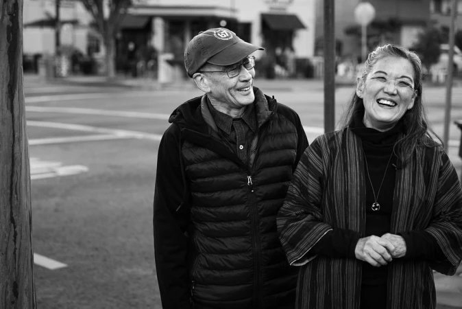 Black and white portrait of an older couple laughing together outdoors on a city street by photographer Doug Menuez.
