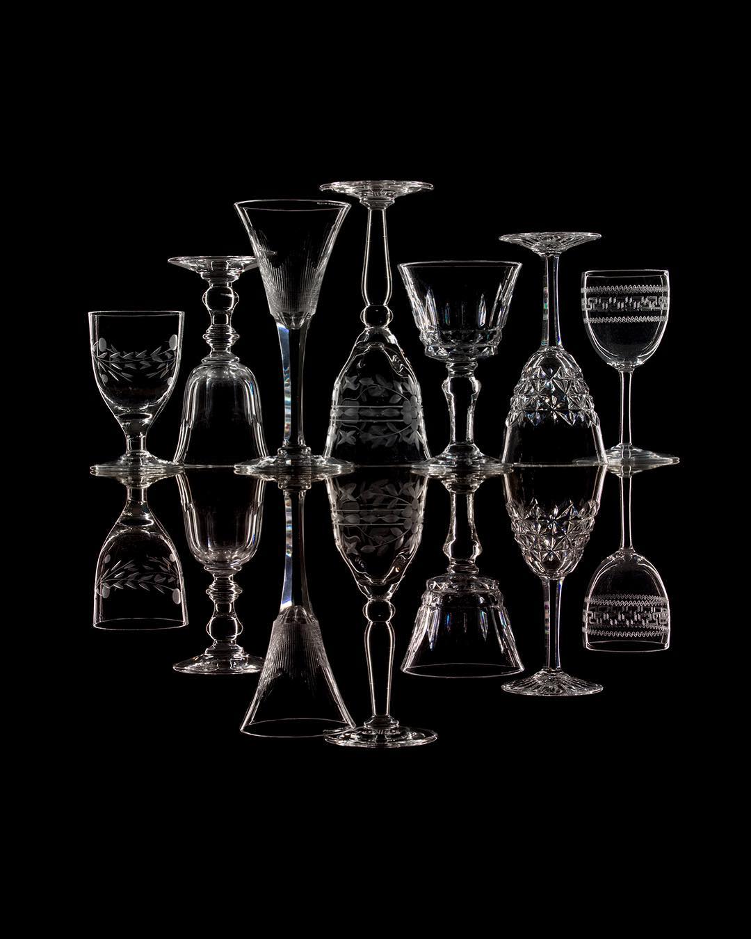 Crystal stemware glasses arranged with reflections on black. Various vintage styles of wine glasses, goblets, and barware.