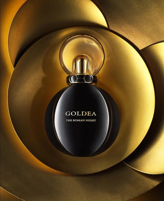 Elegant black perfume bottle on a textured gold surface with the words 'Goldea The Roman Night'. Beauty and fragrance product shot.