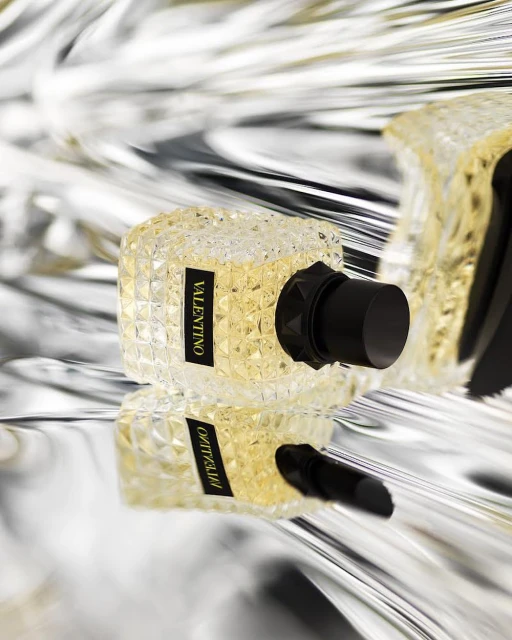 Valentino perfume bottle displayed on a reflective surface, crystal clear bottle with black cap, elegant and luxurious fragrance.