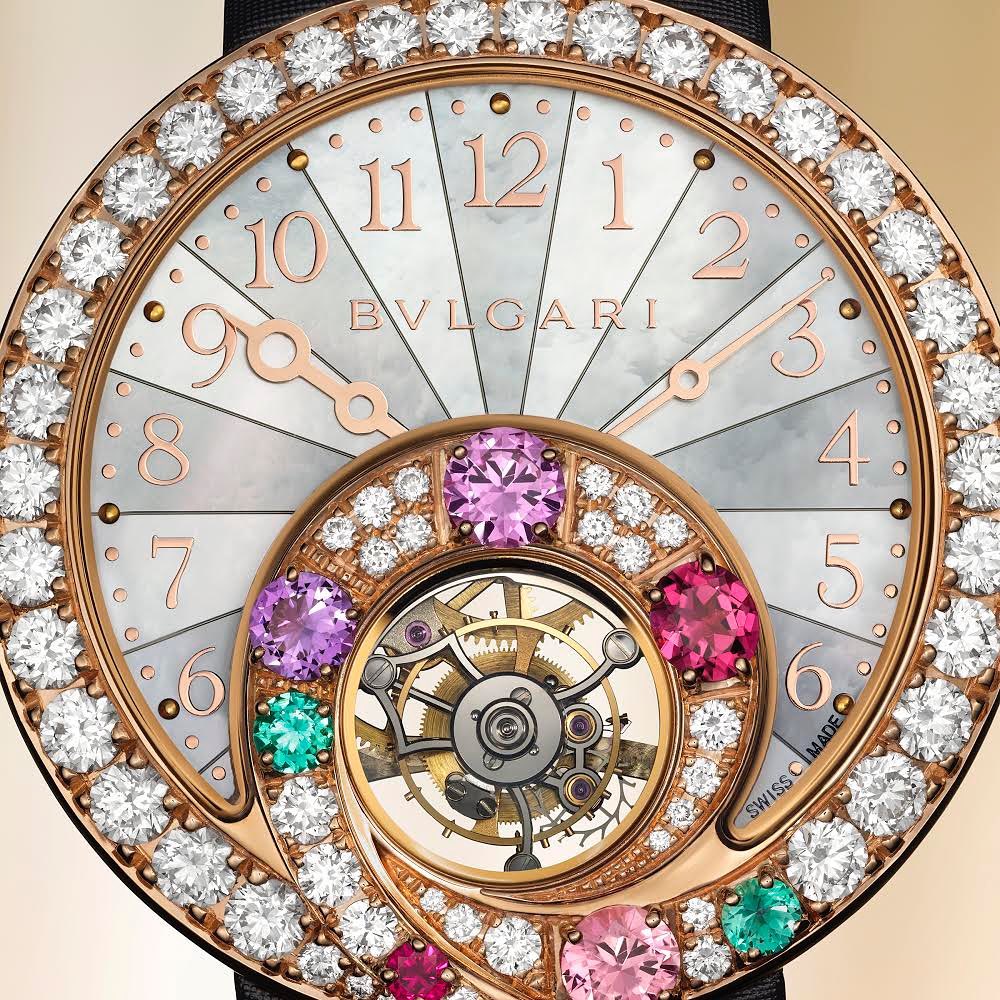 Close-up of a Bulgari wristwatch featuring a mother-of-pearl face, diamond bezel, pink-gold hands, and multicolored gemstones.