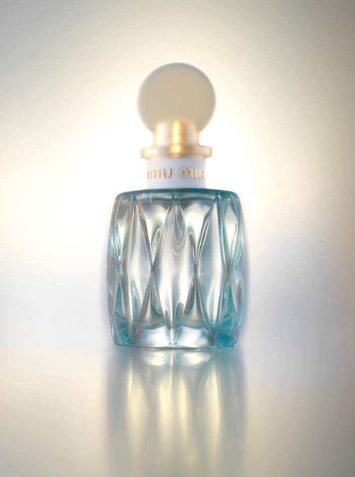 Crystal perfume bottle with circular top and faceted design, centered in a studio shot, illuminated by bright white and gold lighting.