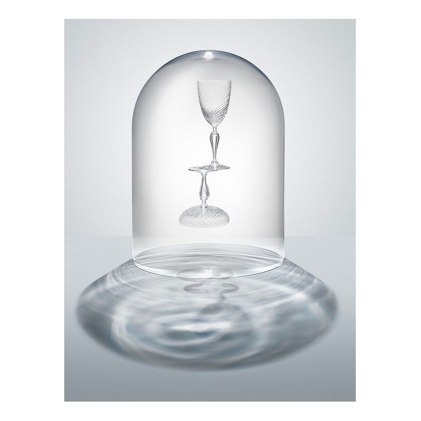 Two wine glasses under a clear cloche dome, displayed on a light grey surface with a rippled shadow pattern.