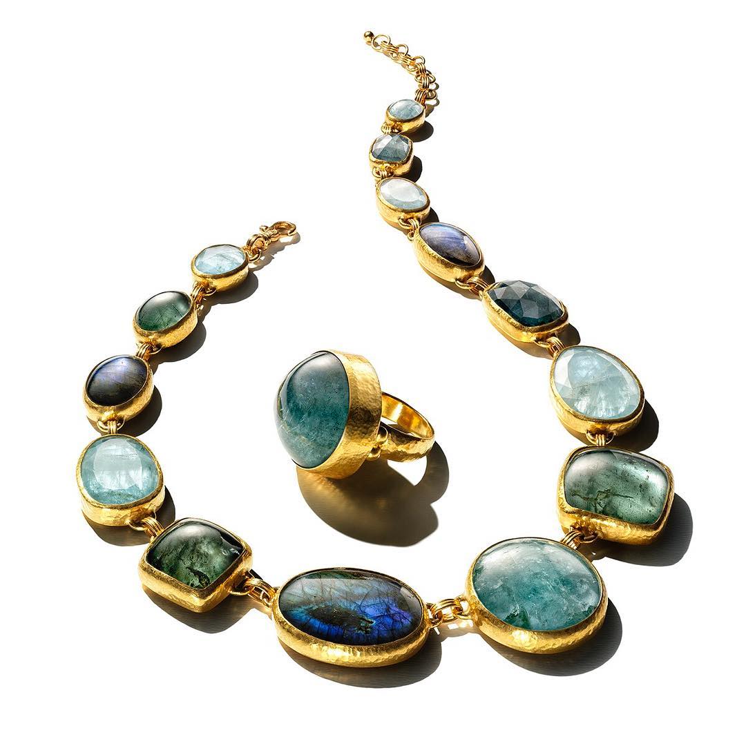 Gold necklace with aqua and green gemstones alongside a matching ring, presented on a white background, illuminated by studio lighting.