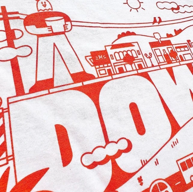 T-shirt featuring a graphic design with a cartoon-like human figure, building outlines, and the word "DOWNTOWN" in bold, red letters.