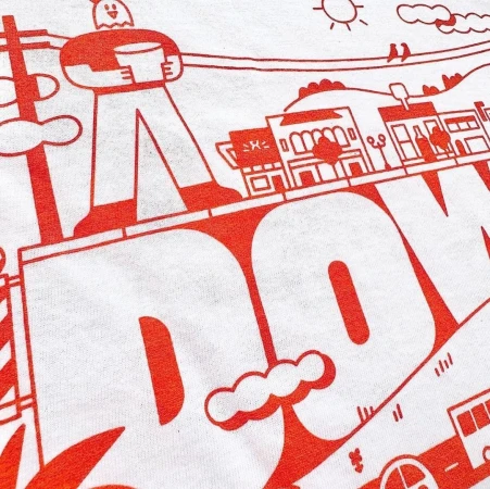 T-shirt featuring a graphic design with a cartoon-like human figure, building outlines, and the word "DOWNTOWN" in bold, red letters.