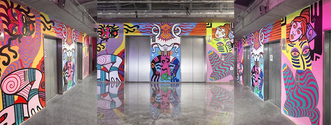 Hallway with vibrant mural art covering the walls, featuring colorful abstract shapes and figures near elevator doors in an indoor setting.