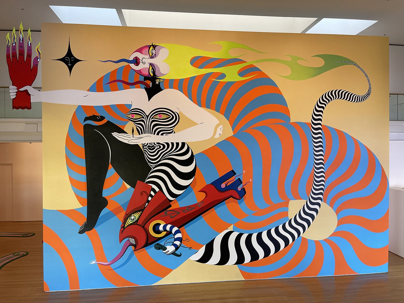 Large mural on the wall depicts a stylized human figure with surreal elements and bold orange, blue, and black-and-white patterned accents.