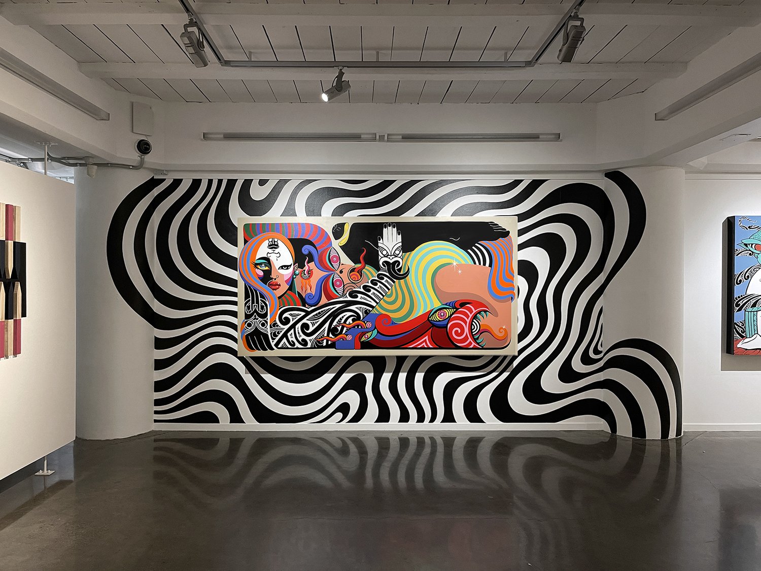 Gallery interior featuring colorful abstract artwork on a wall with bold black and white striped mural background, museum or art exhibit.