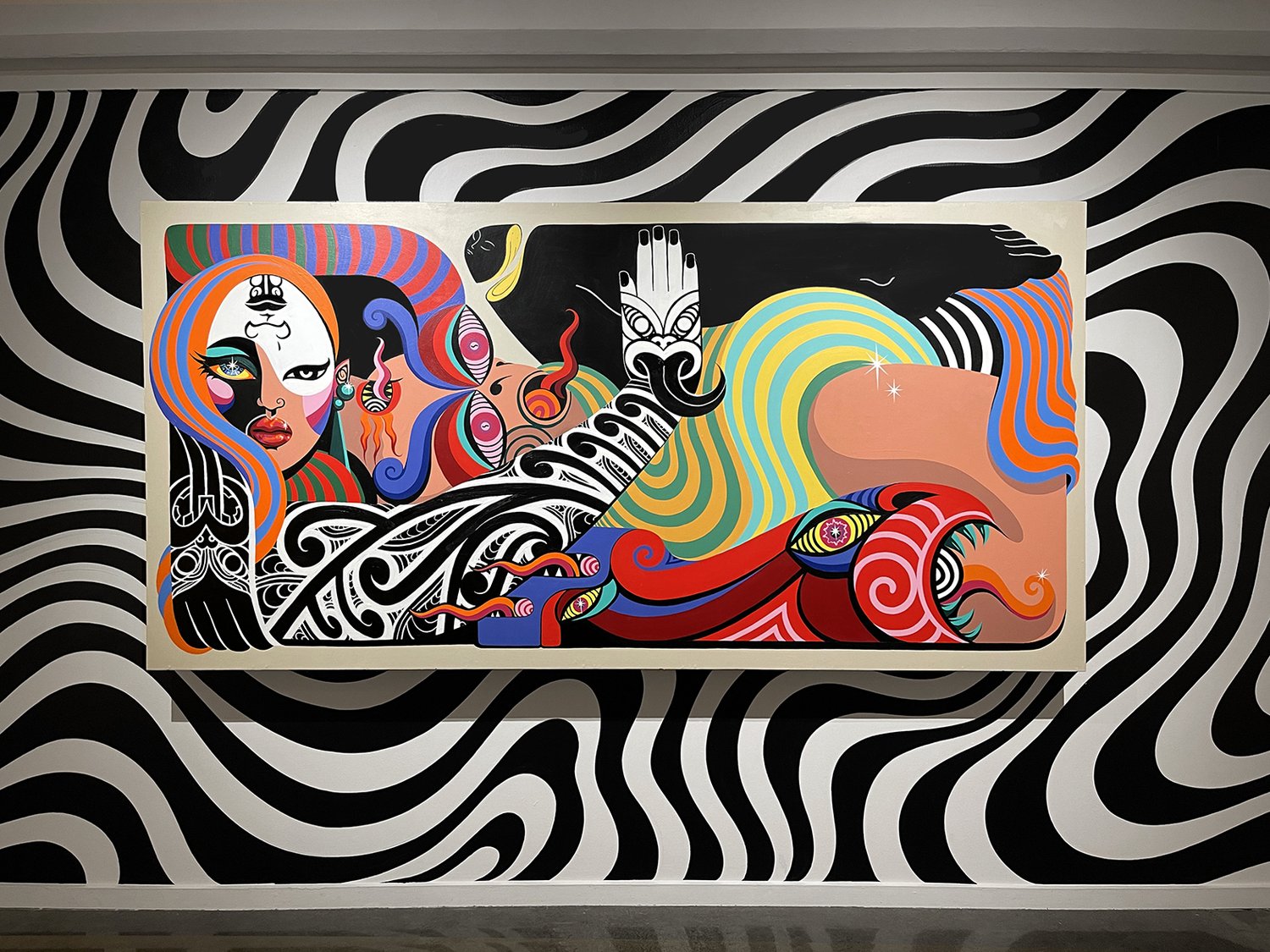 Colourful painting featuring figures, abstract patterns, and design elements on a black and white patterned wall in an indoor setting.
