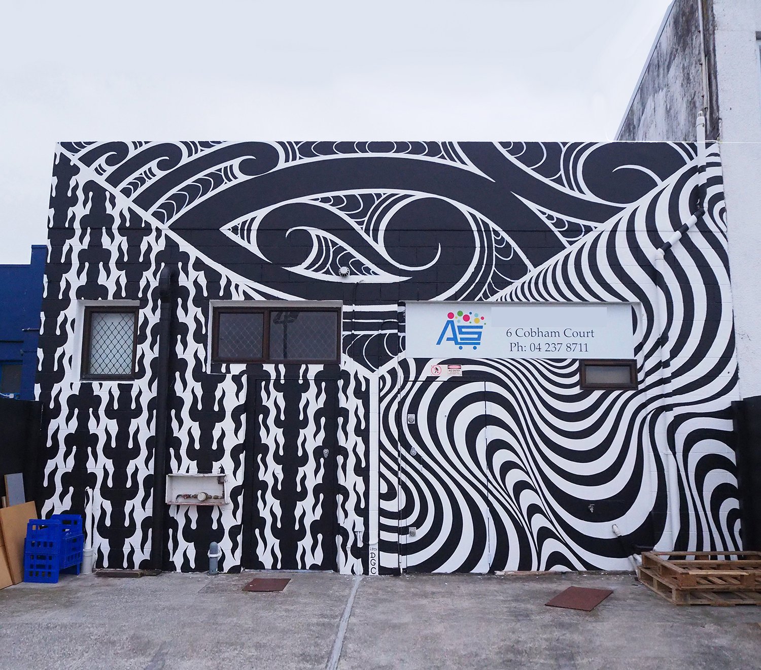 Building exterior showcasing Maori-inspired mural with black and white patterns, including spiral designs and geometric elements under a cloudy sky.