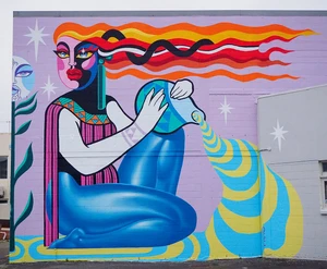 Mural of a stylized woman pouring water from a vessel against a purple background, created by Dream Girls Art Collective.