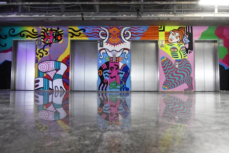 Four elevator doors framed by a large colourful graffiti mural with abstract figures on a glossy concrete floor.