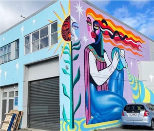 Colorful mural on a building exterior featuring a stylized female figure, a split sun and moon motif, and sparkling stars.