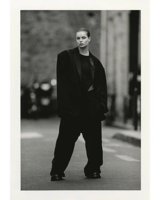A fashion shot of a woman in an oversized suit standing on a city street, rendered in black and white with a shallow depth of field.