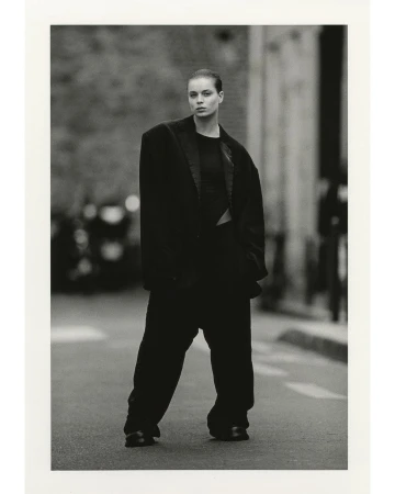 A fashion shot of a woman in an oversized suit standing on a city street, rendered in black and white with a shallow depth of field.