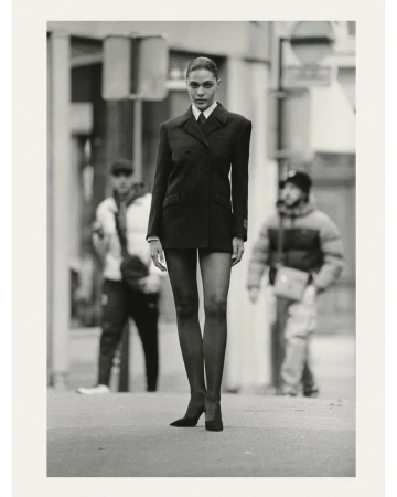 Fashionable woman in suit walks on city street. She has long legs and wears heels. Two blurred people in the background.