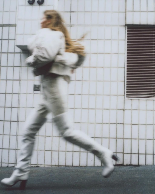 Woman in white outfit running on city street with motion blur and side view in urban setting with geometric tiled building background.