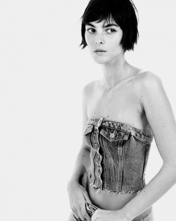 Model with dark bob haircut wearing a strapless denim corset top against a white background by Drew Vickers