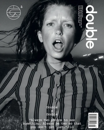 Monochromatic portrait of a young person with an open mouth, wearing a striped shirt, set against a blurred cityscape at dusk.