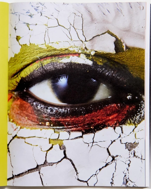 Close-up of a human eye with dramatic makeup, gold eyeshadow, and cracked face paint giving an artistic, textured, and surreal impression.
