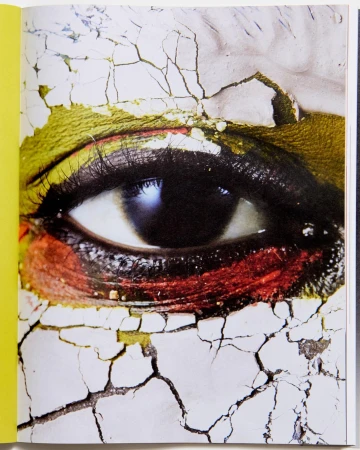 Close-up of a human eye with dramatic makeup, gold eyeshadow, and cracked face paint giving an artistic, textured, and surreal impression.