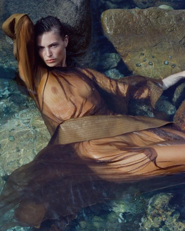 Model lying in clear shallow water wearing a sheer brown dress among wet rocks, photographed by Drew Vickers.