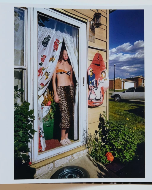 Woman in animal print bikini and pants stands in doorway with patterned curtains on a sunny day with blue skies in an outdoor shot.