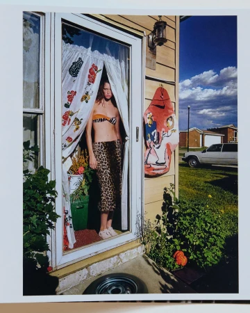 Woman in animal print bikini and pants stands in doorway with patterned curtains on a sunny day with blue skies in an outdoor shot.
