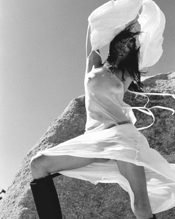 Model in sheer white dress posing on a rocky outcrop outdoors photographed by Drew Vickers in black and white.