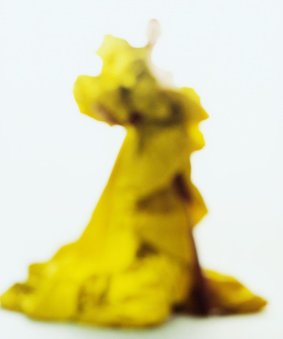 Abstract macro shot of a yellow object or substance against a white background, creating an otherworldly, blurred effect.