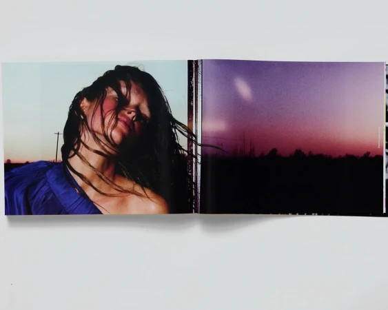 Open photobook displaying a portrait of a woman in a blue top with blowing hair alongside a dusk landscape