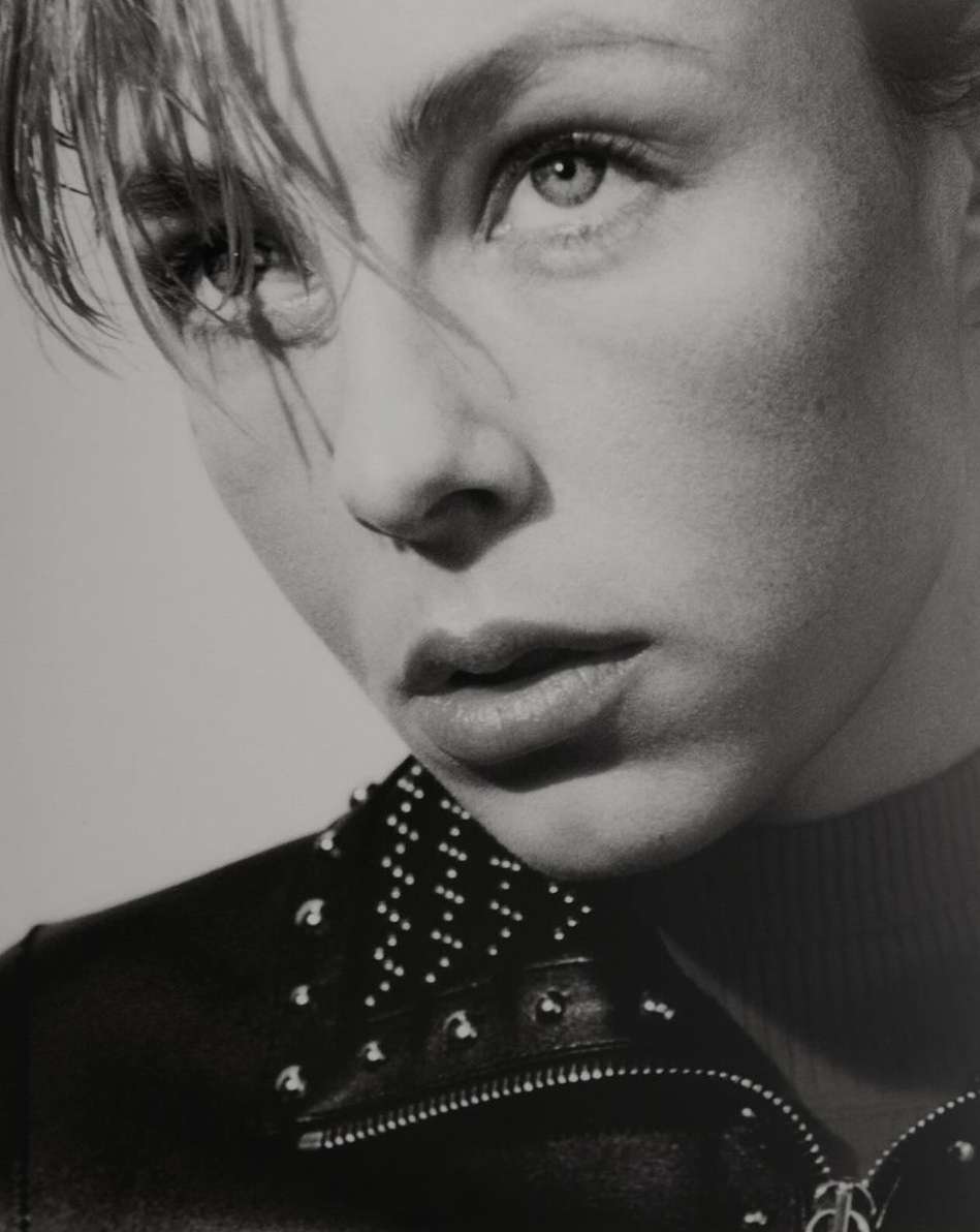 Monochrome portrait of a young woman with short blonde hair and a studded leather jacket against a neutral background, studio lighting.