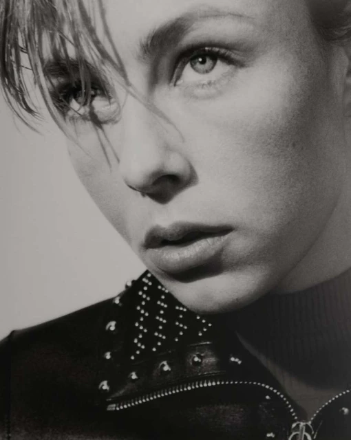 Monochrome portrait of a young woman with short blonde hair and a studded leather jacket against a neutral background, studio lighting.